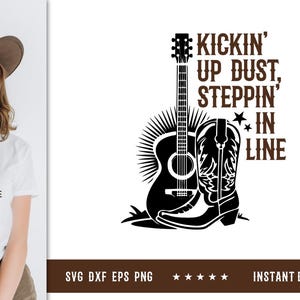 Könnte beinhalten: Weißes T-Shirt mit einer schwarz-braunen Grafik einer Gitarre, eines Cowboy-Stiefels und dem Text "Kickin' Up Dust, Steppin' In Line". Das Design hat ein Country-Musik- oder Western-Thema.