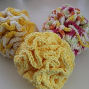 May include: Three crocheted bath poufs in yellow, white, and pink. The poufs are made with a textured, ruffled design.