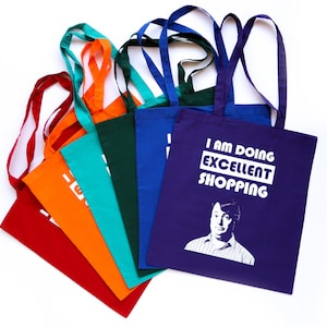 May include: A set of eight colorful tote bags with white text and a graphic of a man. The purple bag has the text "I am doing excellent shopping".