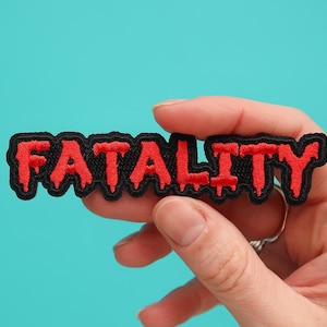 May include: A black and red embroidered patch with the word "FATALITY" in dripping red letters.
