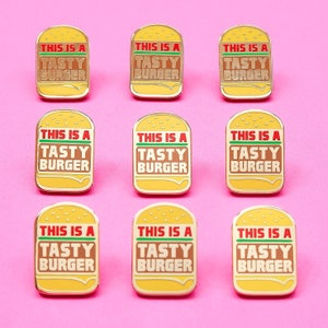 May include: Nine gold-colored enamel pins with a yellow burger design. Each pin says "This is a Tasty Burger" in red and green letters.