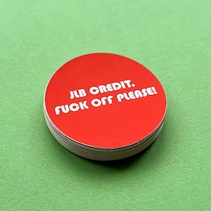 Könnte beinhalten: Ein Stapel roter, runder Aufkleber mit weißem Text. Der Text lautet: "JLB CREDIT. FUCK OFF PLEASE!" Die Aufkleber liegen auf einer grünen Oberfläche.