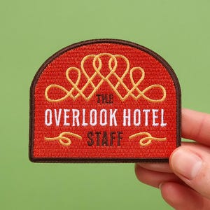 May include: Red embroidered patch with a gold design of interlocking circles and the text "The Overlook Hotel Staff".