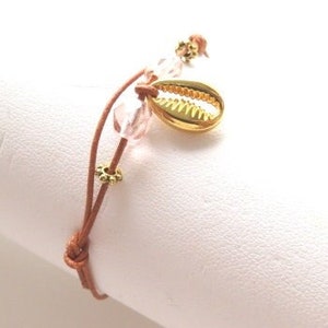 May include: A brown leather bracelet with pink and gold beads and a gold seashell charm.