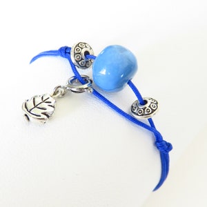 May include: A blue cord bracelet with a silver charm, a blue glass bead, and two silver spacer beads.
