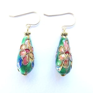 Könnte beinhalten: Ein Paar Ohrhänger mit grünen, tropfenförmigen Perlen aus Emaille. Die Perlen sind mit bunten Blumenmustern und goldenen Akzenten verziert.