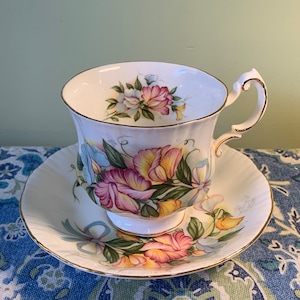 Peut inclure: Une tasse à thé et une soucoupe blanches avec un motif floral. Le motif présente des fleurs roses, jaunes et bleues avec des feuilles vertes. La tasse et la soucoupe ont une bordure dorée.