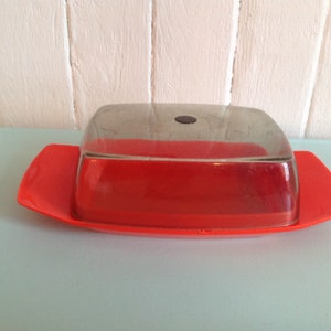 May include: A red plastic butter dish with a clear glass lid. The lid has a black knob on top.