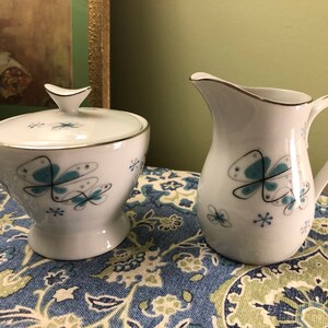Peut inclure: Un ensemble sucrier et crémier blanc avec un motif de papillon bleu et gris. L'ensemble est doté d'une bordure argentée autour du haut.