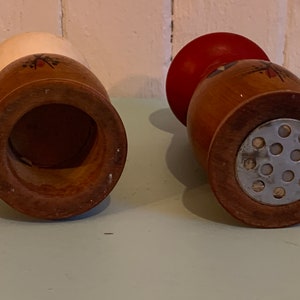 May include: Two wooden salt and pepper shakers with a red and white top and a metal grinder on the bottom.