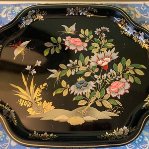 Pu&ograve; includere: Vassoio da portata in metallo nero con bordo dorato e un motivo floreale con farfalle, fiori e foglie in tonalit&agrave; di rosa, bianco, blu e verde. Il vassoio ha le parole "Fine Wooden Tray" stampate sul fondo.