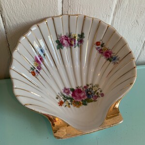Peut inclure: Un plat en forme de coquille de porcelaine blanche avec un bord doré et un motif floral. Le plat est décoré de fleurs roses, rouges, jaunes et bleues.