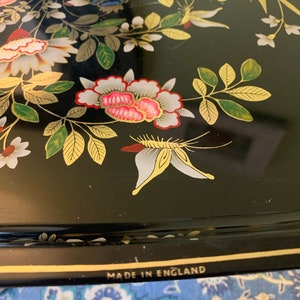 Pu&ograve; includere: Vassoio in metallo nero con bordo dorato e design floreale. Il vassoio presenta una farfalla bianca e le parole "Made in England" sul fondo.