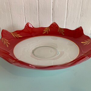 Peut inclure: Un bol de service en céramique rouge avec un intérieur blanc et des accents de feuilles d'or. Le bol a un bord festonné et un centre surélevé.