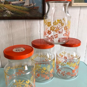 Puede incluir: Cuatro tarros de vidrio con tapas naranjas y dise&ntilde;os florales en tonos amarillos y naranjas. Los tarros est&aacute;n etiquetados con "Banka 8G12".