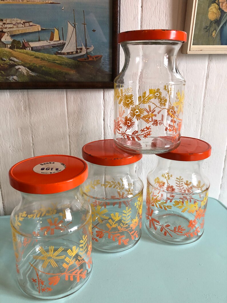 Puede incluir: Cuatro tarros de vidrio con tapas naranjas y dise&ntilde;os florales en tonos amarillos y naranjas. Los tarros est&aacute;n etiquetados con "Banka 8G12".
