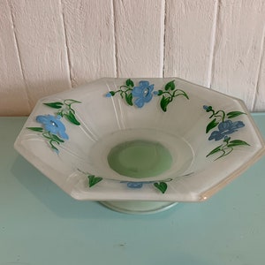 May include: A white octagonal glass bowl with a green base and blue floral designs. The bowl has a raised base.