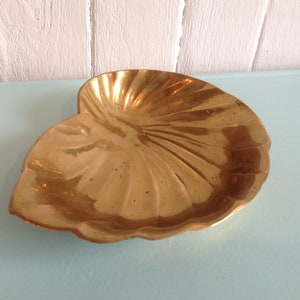 Peut inclure: Un plat en métal doré en forme de coquille Saint-Jacques. Le plat a une surface lisse et brillante et un bord festonné.