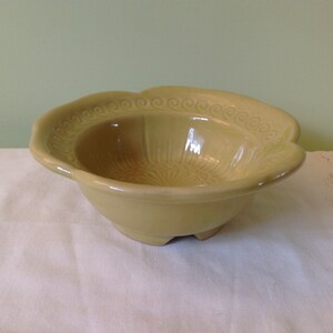 Peut inclure: Un petit bol en céramique jaune avec un motif décoratif autour du bord et un motif texturé sur le fond. Le bol a un bord festonné et repose sur trois petits pieds.