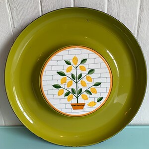 Peut inclure: Un plateau de service en métal vert avec une section centrale amovible. La section centrale présente un mur de briques blanches avec un citronnier jaune dans un pot brun. L'arbre a des feuilles vertes et des citrons jaunes.