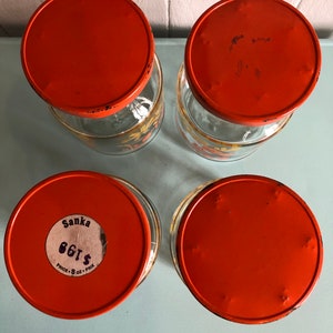 Puede incluir: Cuatro tarros de vidrio naranja con tapas. Los tarros tienen un dise&ntilde;o floral y las tapas son de un naranja brillante. Un tarro tiene una etiqueta que dice "Sanka 86&cent; PRICE: 8 OZ. - PRIX"