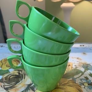 May include: Set of four green ceramic mugs with a unique curved design and a handle. The mugs are stacked on top of each other.