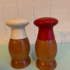 May include: A set of two wooden salt and pepper shakers. The shakers are shaped like a chef's hat. One shaker is painted white and the other is painted red.