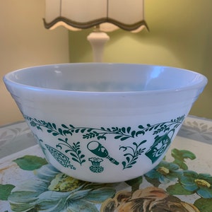 Peut inclure: Bol en céramique blanc avec un motif floral vert représentant des ustensiles de cuisine. Le bol a un bord festonné.