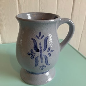 Peut inclure: Une tasse en céramique bleu clair avec un motif floral bleu. La tasse a une anse et une base arrondie.