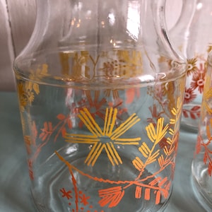 Puede incluir: Conjunto de cuatro tarros de vidrio transparente con tapas rojas y un dise&ntilde;o floral en naranja y amarillo. Los tarros son perfectos para guardar especias, hierbas u otros art&iacute;culos esenciales de cocina.