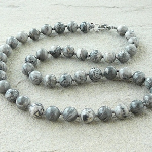 Puede incluir: Un collar de cuentas de piedra marmoleada gris y blanca. Las cuentas son redondas y tienen un aspecto natural y orgánico. El collar mide aproximadamente 45 cm de largo.