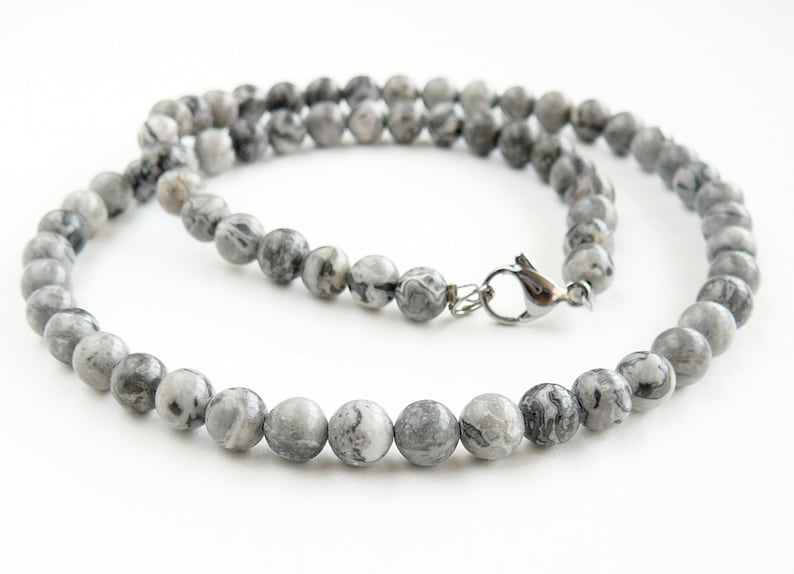 May include: A gray and white stone beaded necklace with a silver clasp.