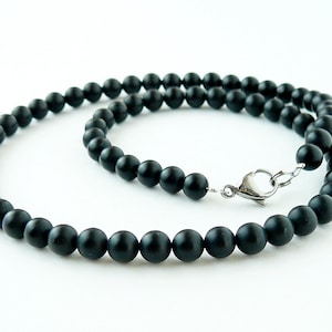May include: A black beaded necklace with a silver clasp. The beads are round and matte.