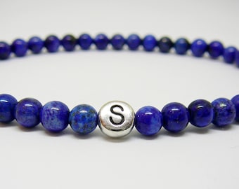 May include: A blue lapis lazuli beaded bracelet with a silver charm bead that has the letter "S" on it.