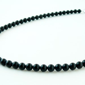 May include: A black beaded necklace with a silver clasp. The beads are round and matte.
