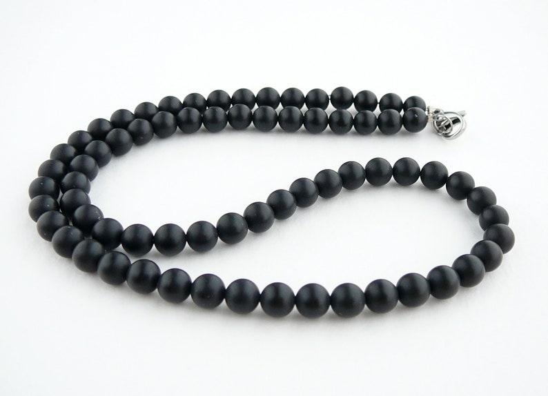 May include: A black beaded necklace with a silver clasp. The beads are round and matte.