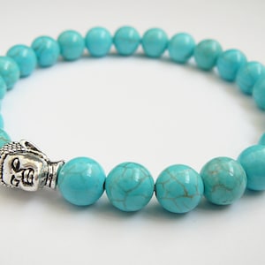 May include: Turquoise blue beaded bracelet with a silver Buddha head charm.