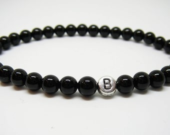 May include: Black beaded bracelet with a silver charm bead that has the letter "B" on it.