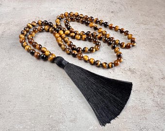 May include: A beaded necklace with tiger's eye stones and a black tassel. The necklace features round, polished beads in shades of brown and gold. The black tassel is made of silky threads.