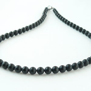 May include: A black beaded necklace with a silver clasp. The beads are round and smooth.