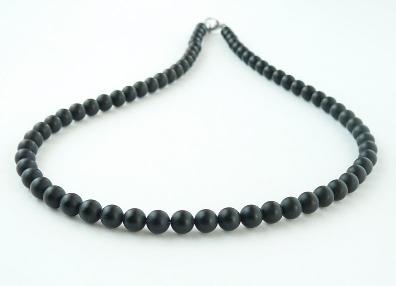 May include: A black beaded necklace with a silver clasp. The beads are round and smooth.