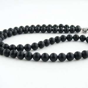 May include: A black beaded necklace with a silver clasp. The beads are round and matte.