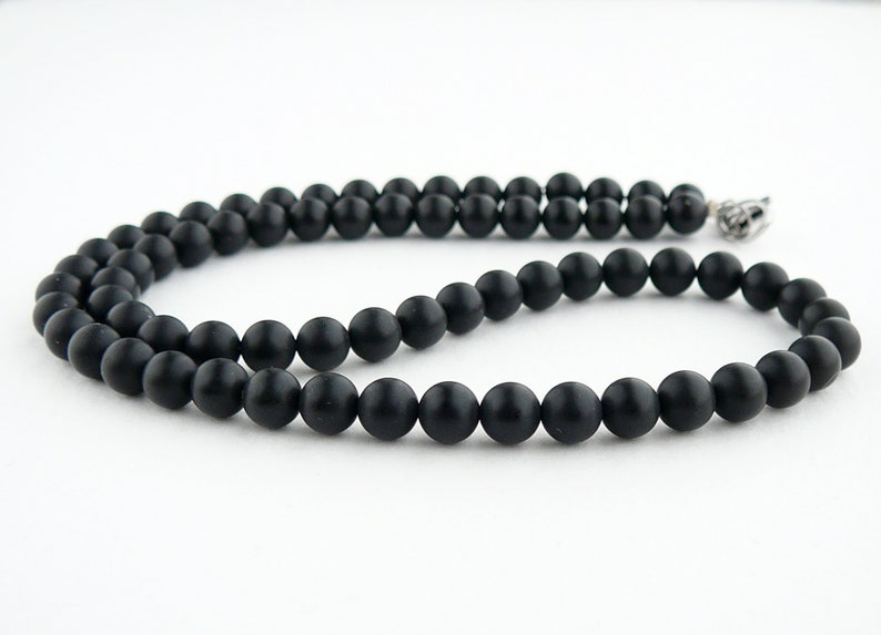 May include: A black beaded necklace with a silver clasp. The beads are round and matte.