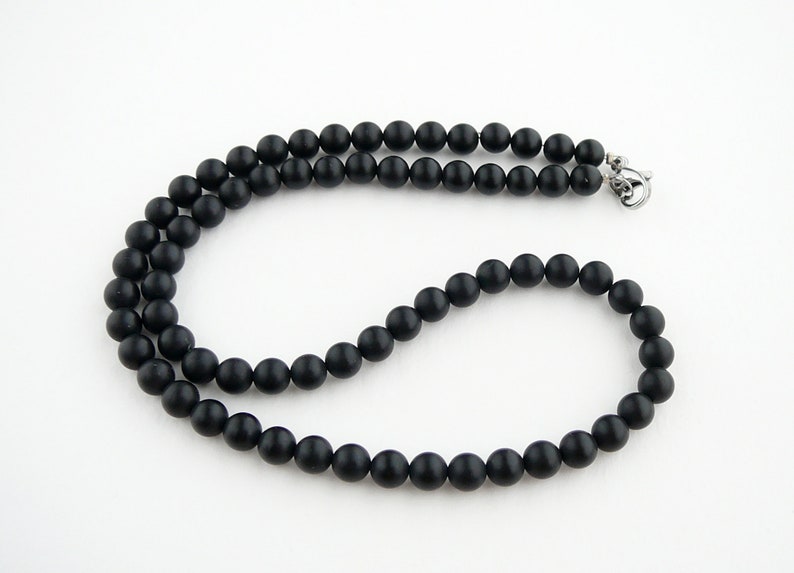 May include: A black beaded necklace with a silver clasp. The beads are round and matte.