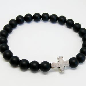 May include: A black beaded bracelet with a silver cross charm. The beads are matte and round.