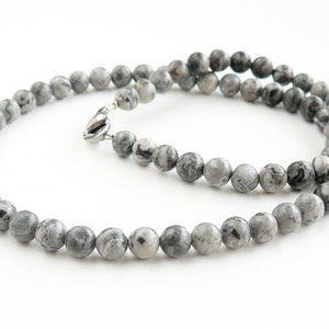 May include: A gray and black marbled stone beaded necklace with a silver clasp.