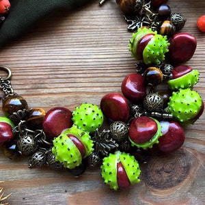 Könnte beinhalten: Ein braunes Lederarmband mit grünen und braunen Perlen, darunter Tigerauge-Perlen, und einem herzförmigen Verschluss. Das Armband verfügt über eine Vielzahl von Charms, darunter Blätter und kleine runde Perlen.