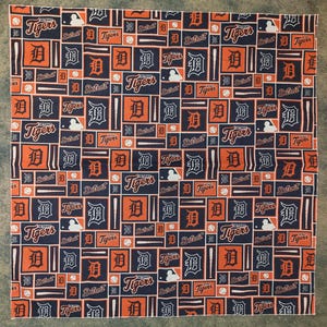 May include: A blue and orange bandana with a repeating pattern of the Detroit Tigers logo, baseball bats, and the words "Detroit Tigers".