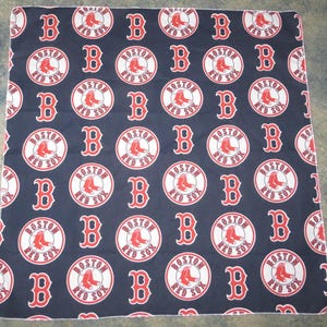 May include: A dark navy blue fabric blanket featuring a repeating pattern of the Boston Red Sox circular logo in red and white, interspersed with large red letter B symbols printed across the entire surface of the textile material.