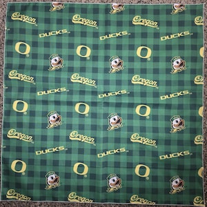 Puede incluir: Tela de cuadros verdes y negros con el logotipo de los Oregon Ducks, la palabra "Oregon", la palabra "DUCKS" y la letra "O". La tela tiene un patrón repetido de la mascota de los Oregon Ducks.
